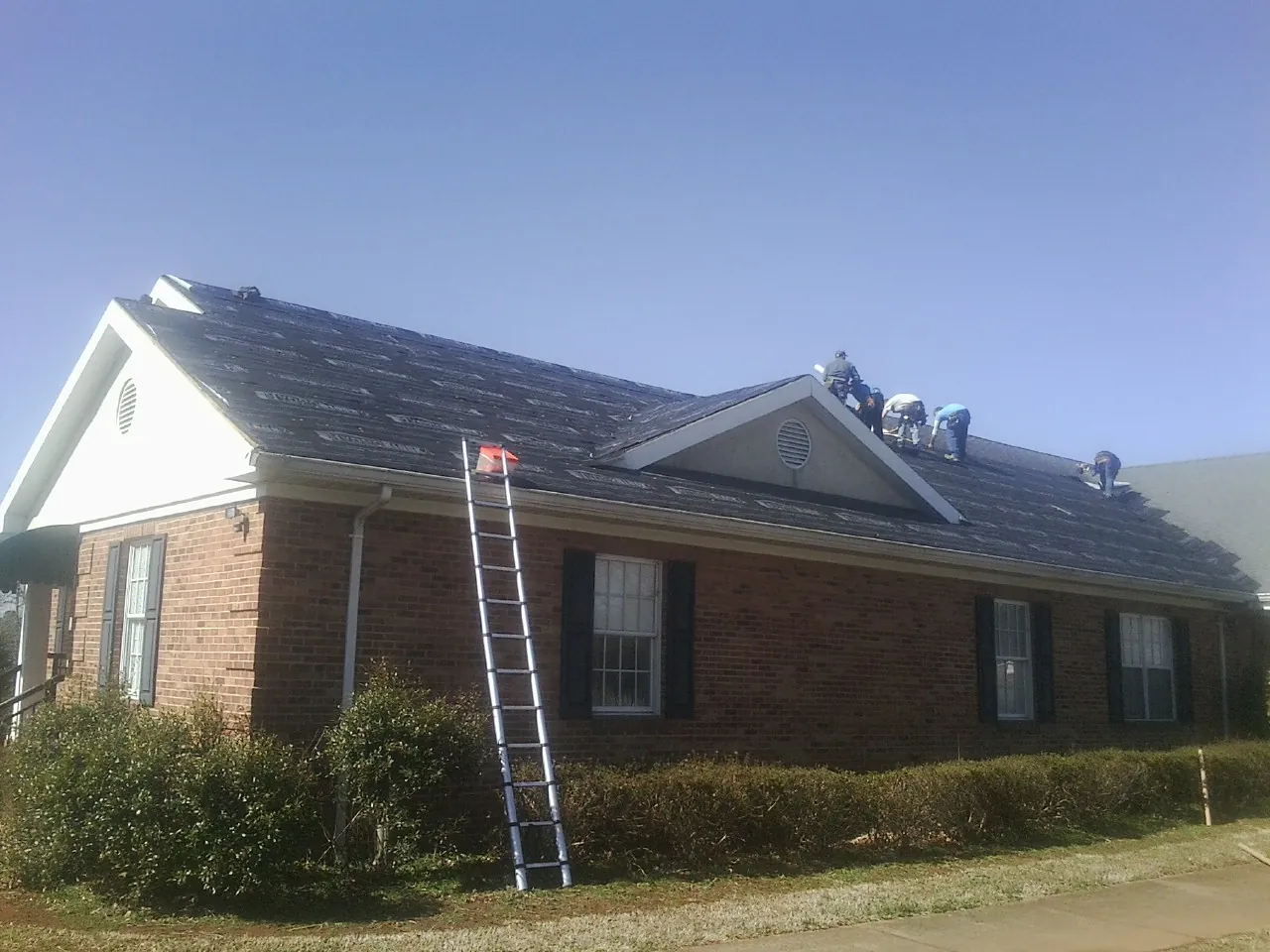 Crew tearing shingles off a brick ranch roof with a ladder set — Metal Roof Repair work by our crew in New Carlisle
