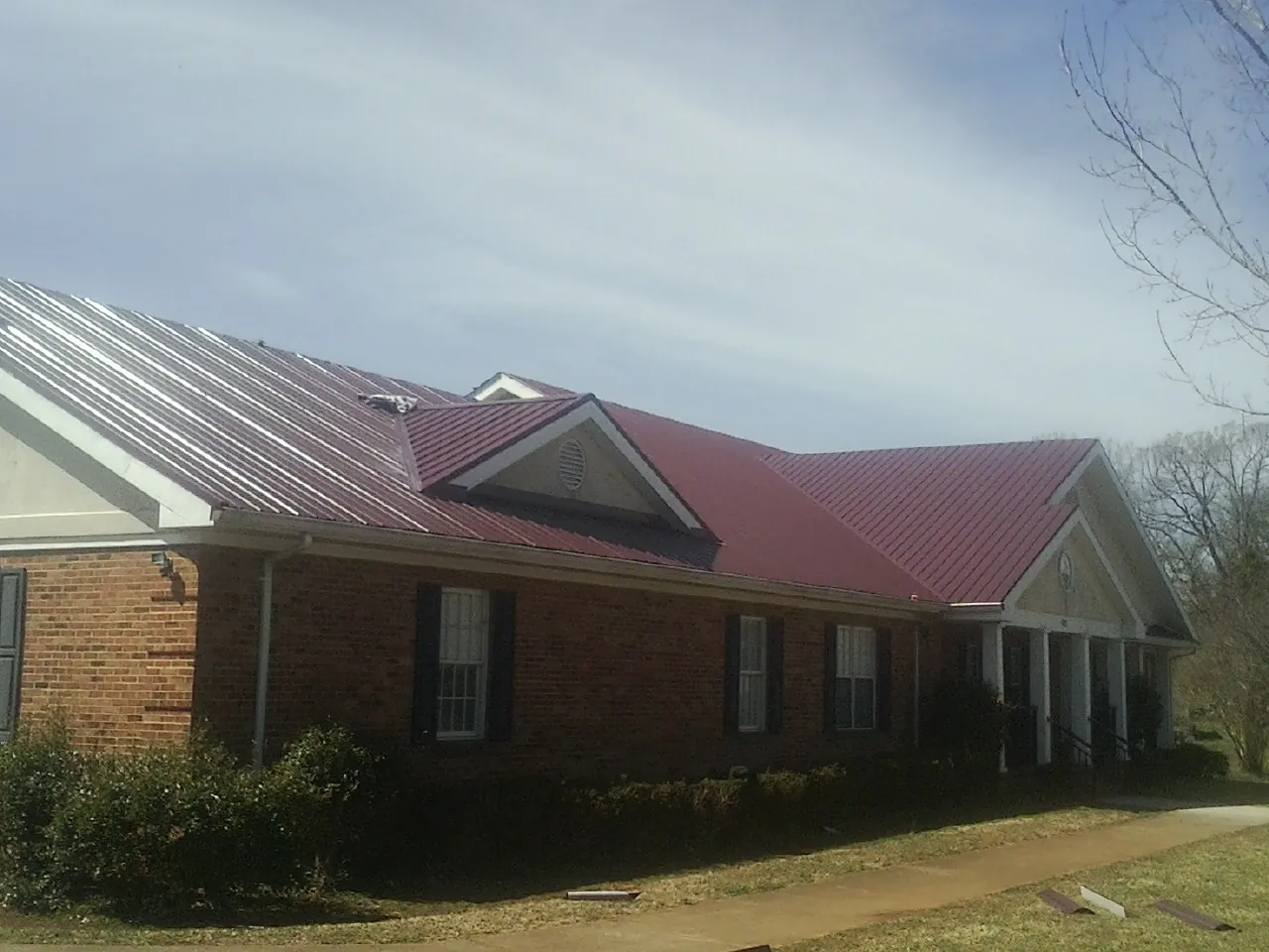Red metal roof with gabled entries on a long brick building, from a Hail Damage Roof Repair job in New Carlisle