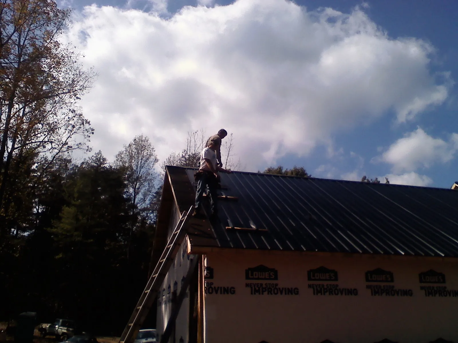 Roofer fastening dark metal panels high against a cloudy sky, from a Roof Inspection job in New Carlisle