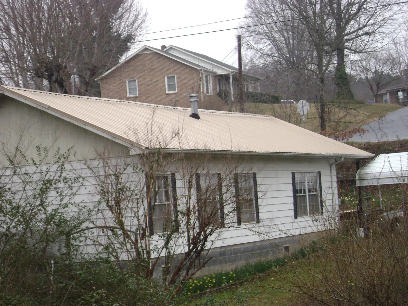 Tan metal roof on a white sided house set into a hillside — Commercial Roofing by Roofing Brothers in New Carlisle