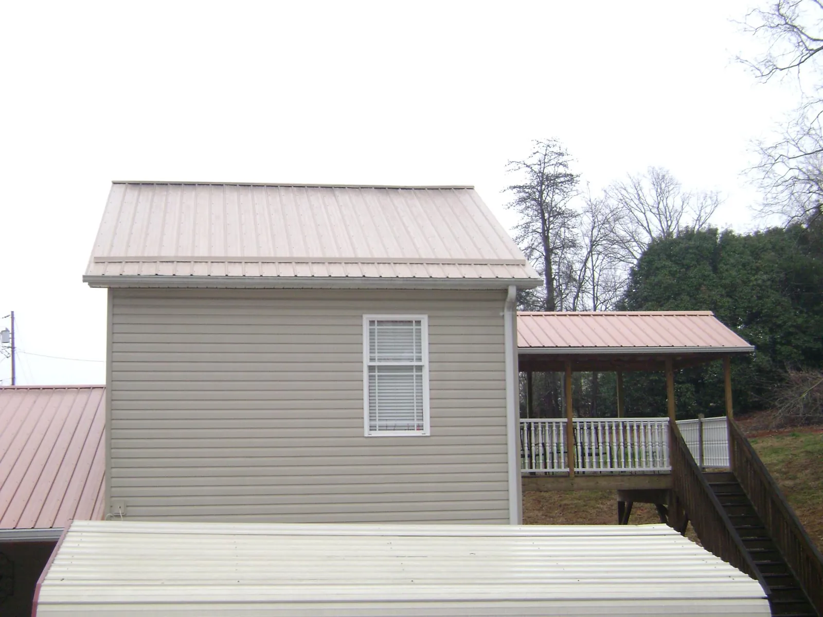 Tan metal roofs on a two story addition and attached porch, from a Roof Replacement job in New Carlisle